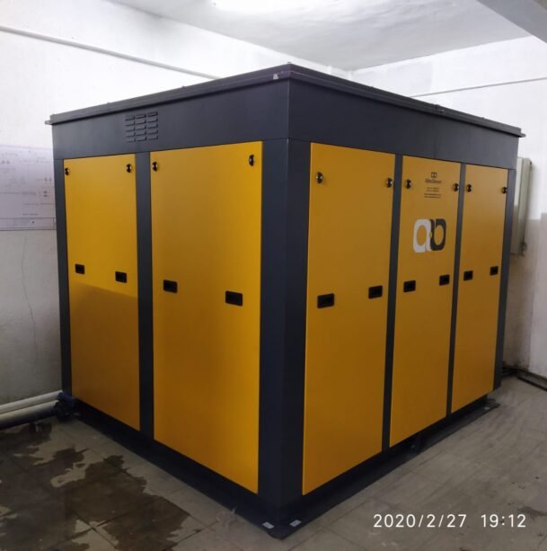 Large yellow and grey acoustic enclosure with forced ventilation installed around blowers in a plant room
